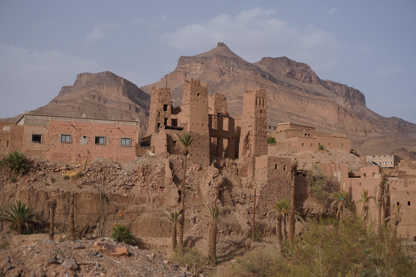 Morocco weather in the south: old adobe ksar and palm trees below desert mountains in the Draa Valley